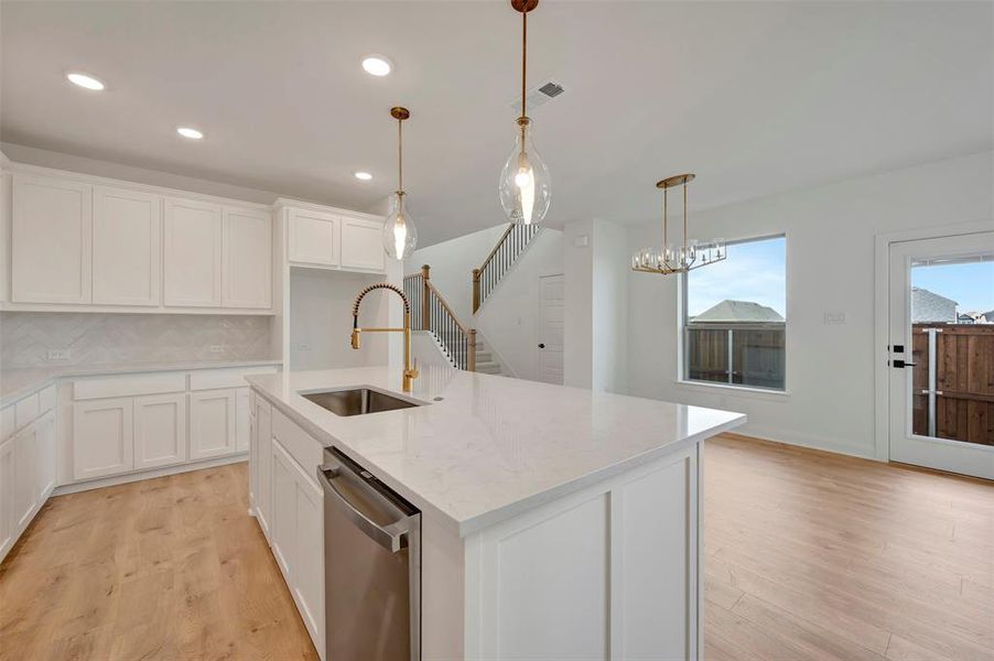 Kitchen with an island with sink, white cabinetry, stainless steel dishwasher, light wood finished floors, and light stone counters