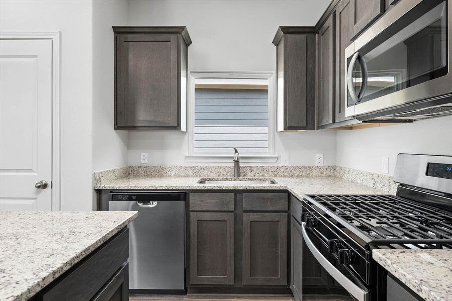 Kitchen featuring appliances with stainless steel finishes, light stone countertops, dark brown cabinetry, and light wood-style floors Kitchen featuring appliances with stainless steel finishes, light stone countertops, dark brown cabinetry, and light wood-style floors