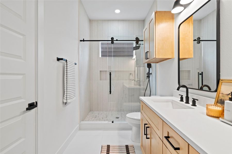 Walk-in shower boasts vertical tile for a sense of height, a built-in niche for streamlined storage, and a matte black rain showerhead and wand for luxe daily rituals.