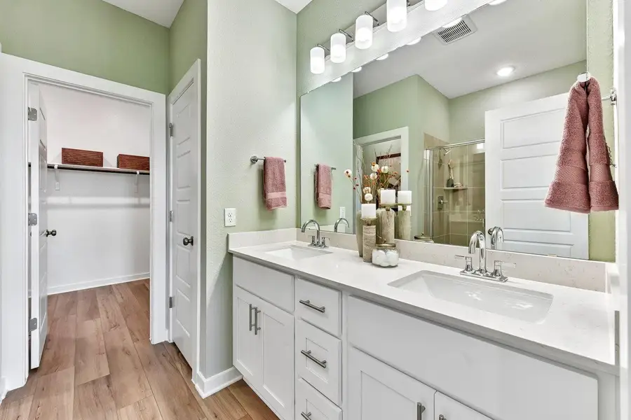 Double vanities with stone countertops stand adjacent to a spacious walk-in closet. Double vanities with stone countertops stand adjacent to a spacious walk-in closet.