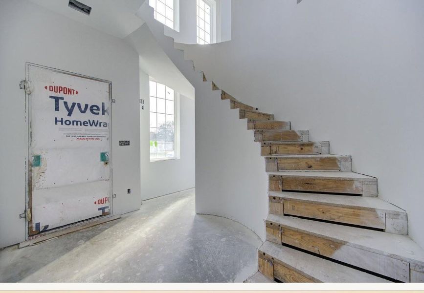 Dramatic two-story foyer with an elegant curved staircase and expansive windows that create a welcoming entrance.