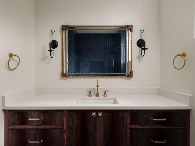 A dark wood vanity with a white countertop and brass fixtures enhances this elegant bathroom.