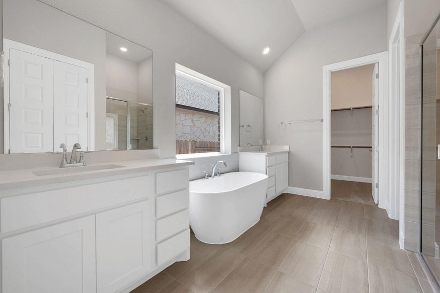 Bathroom featuring a stall shower, lofted ceiling, two vanities, a freestanding tub, and a walk in closet