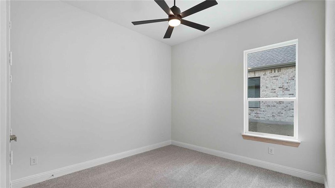 Bright interior space featuring light gray walls, plush gray carpeting, a modern ceiling fan with integrated lighting, and a white-framed window with a wood-finish sill