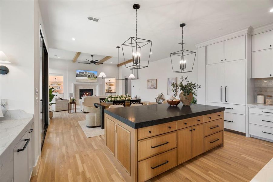 Kitchen with light wood-style floors, a lit fireplace, ceiling fan, open floor plan, and beamed ceiling Kitchen with light wood-style floors, a lit fireplace, ceiling fan, open floor plan, and beamed ceiling