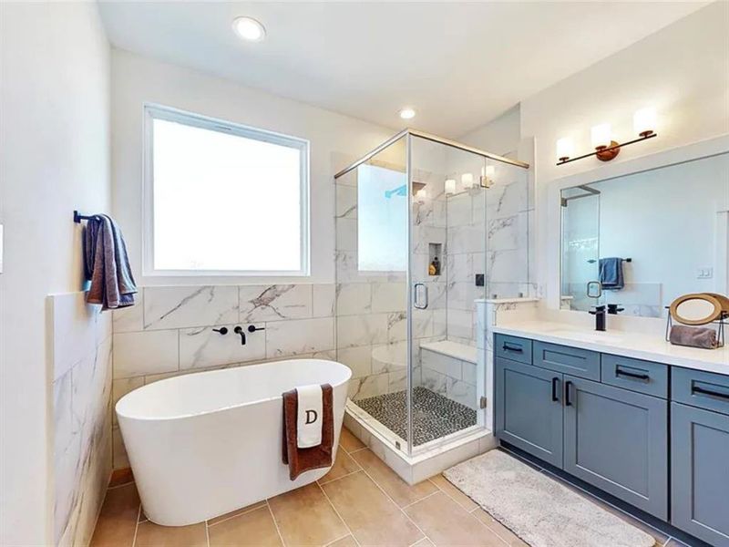 A modern bathroom with a white bathtub, a walk-in shower, and a vanity. The bathroom has white subway tiles with gray veining throughout. The walls are a light cream color, and the lighting is bright. There is a window above the bathtub, letting in natural light.