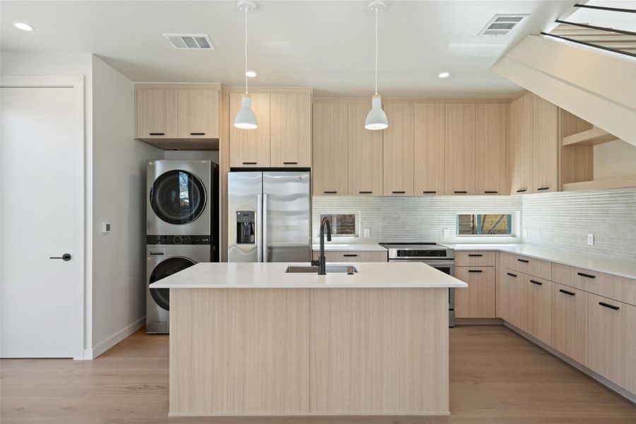 Kitchen with appliances with stainless steel finishes, stacked washer / drying machine, visible vents, and light brown cabinetry