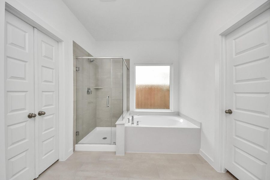 Escape to a spa-like oasis in this primary bathroom. Enjoy a walk-in shower with tile surround, a separate garden tub with custom detailing, and an elegant vanity featuring light countertops, modern hardware, and beautiful recessed lights. Experience luxury and relaxation in every detail. Sample photo of completed home with similar floor plan. Actual colors and selections may vary.