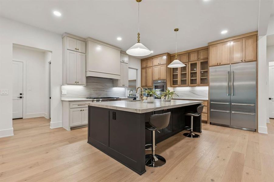 Kitchen with built in fridge, hanging light fixtures, light wood-style floors, a kitchen bar, and recessed lighting