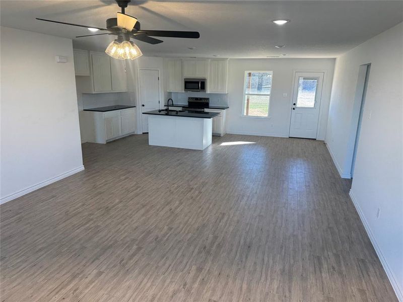 Kitchen with wood-type flooring, ceiling fan, appliances with stainless steel finishes, white cabinetry, and an island with sink