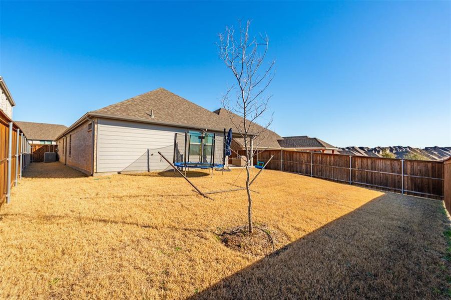 Rear view of property featuring a trampoline, brick siding, a shingled roof, central AC unit, and a fenced backyard