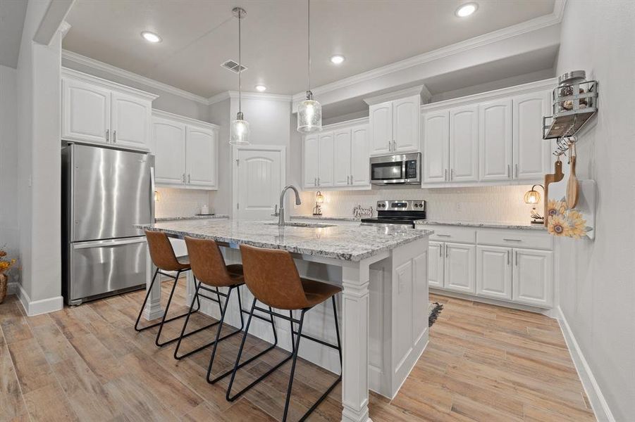 Kitchen featuring light stone countertops, appliances with stainless steel finishes, white cabinetry, backsplash, and crown molding