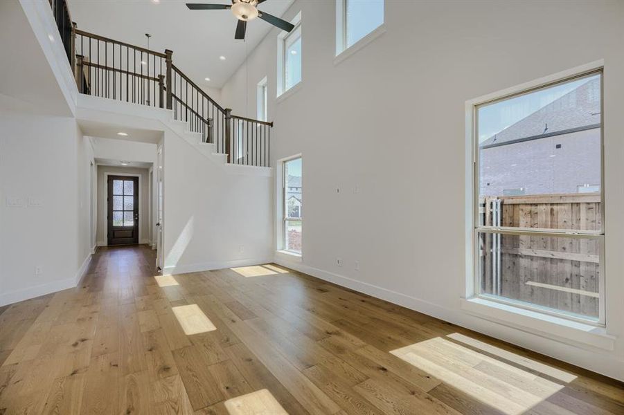 Two-story living area featuring wood-finish flooring, a contemporary ceiling fan, and multiple windows