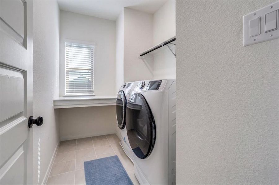 Laundry room with separate washer and dryer, light tile patterned floors, and a textured wall