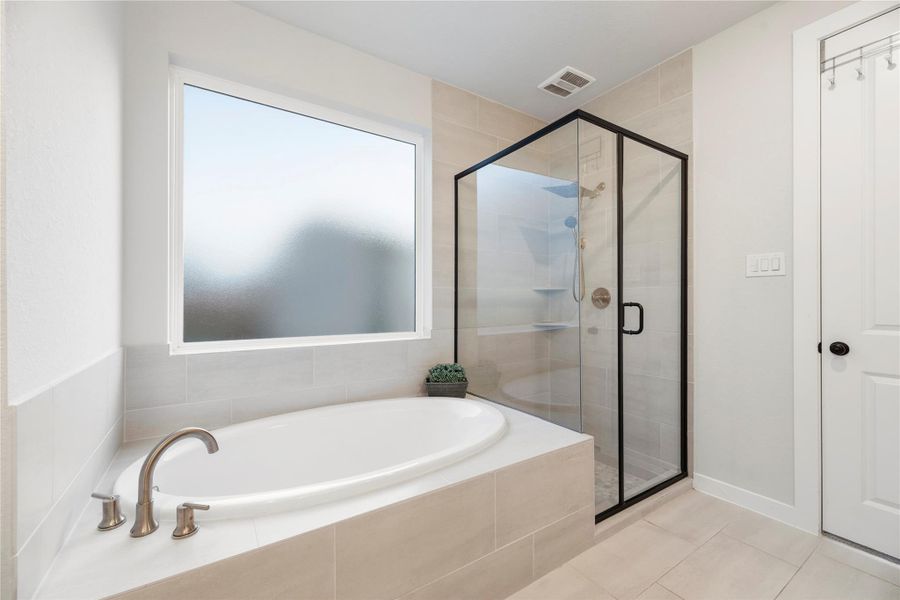 This modern bathroom features a spacious soaking tub and a sleek, glass-enclosed shower with matte black fixtures. The frosted window provides natural light and privacy, creating a serene oasis for relaxation.