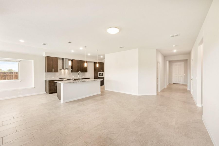 Open-concept kitchen with dark cabinets, white island, pendant lights, and tile floors leading to a hallway