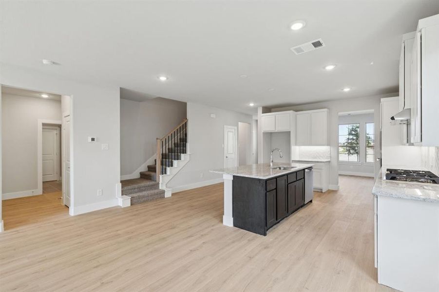 Kitchen with light stone counters, white cabinets, a center island with sink, light wood finished floors, and recessed lighting Kitchen with light stone counters, white cabinets, a center island with sink, light wood finished floors, and recessed lighting