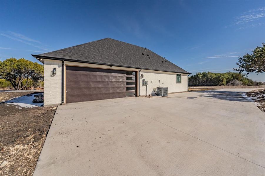View of side of home with driveway, brick siding, roof with shingles, and a garage