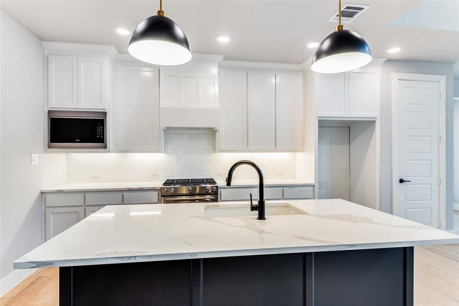 Kitchen with tasteful backsplash, light wood-type flooring, an island with sink, light stone counters, and appliances with stainless steel finishes