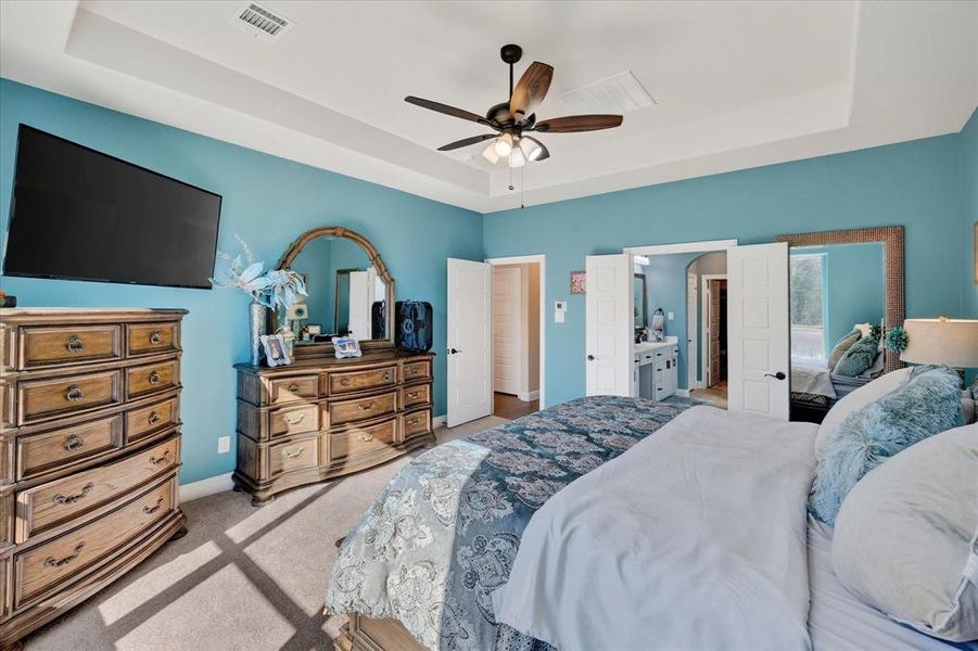 Bedroom with a raised ceiling, carpet, ceiling fan, and connected bathroom Bedroom with a raised ceiling, carpet, ceiling fan, and connected bathroom