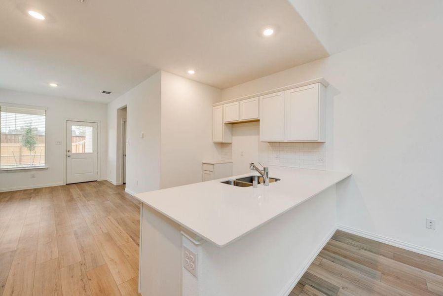 Kitchen featuring light hardwood / wood-style flooring, kitchen peninsula, sink, decorative backsplash, and white cabinets