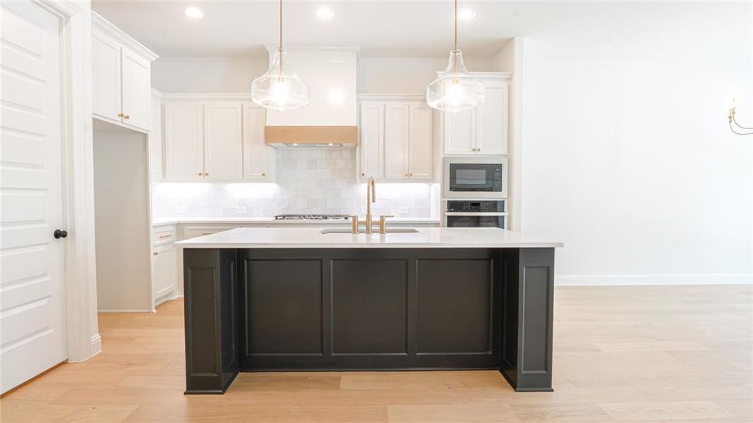 Kitchen featuring white cabinetry, light countertops, an island with sink, tasteful backsplash, and recessed lighting Kitchen featuring white cabinetry, light countertops, an island with sink, tasteful backsplash, and recessed lighting