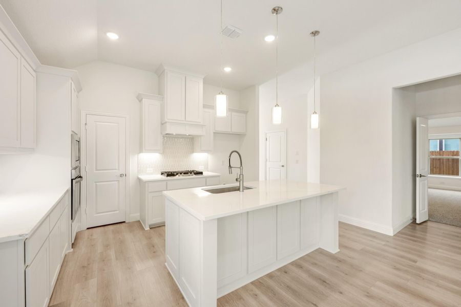 White kitchen with center island, pendant lights, white cabinets, and light wood floors