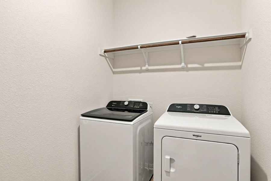 Functional laundry setup includes a high shelf with integrated hanging space.