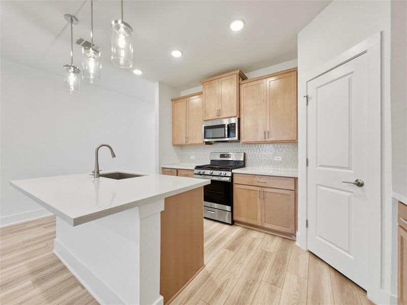 Kitchen featuring stainless steel appliances, light wood-style floors, an island with sink, backsplash, and light wood finish cabinets