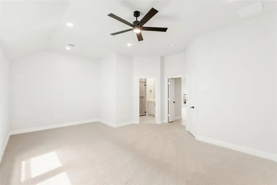 Empty bedroom with vaulted ceiling, ceiling fan, carpet flooring, and doors leading to bathroom and hallway.