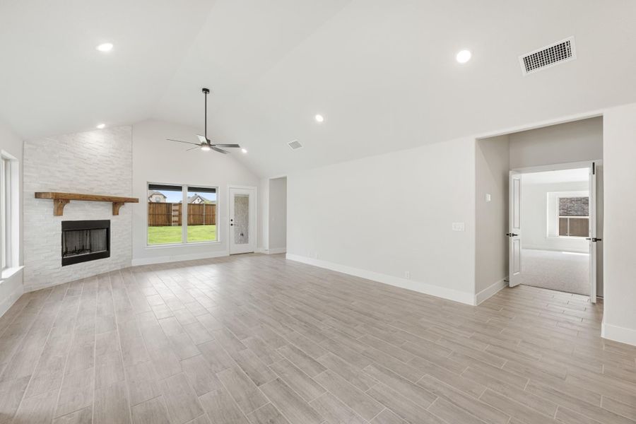 Open living room with vaulted ceiling, stone fireplace, ceiling fan, and light wood-look tile floors