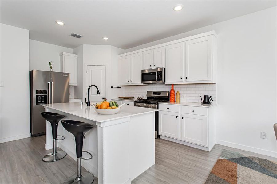 Modern kitchen featuring white cabinetry, a kitchen island with seating, stainless steel appliances, and wood-look flooring