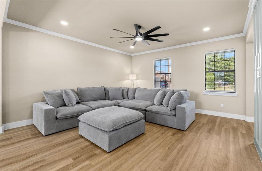 Living area featuring wood-finish flooring, two windows with blinds, a modern ceiling fan, recessed lighting, and crown molding