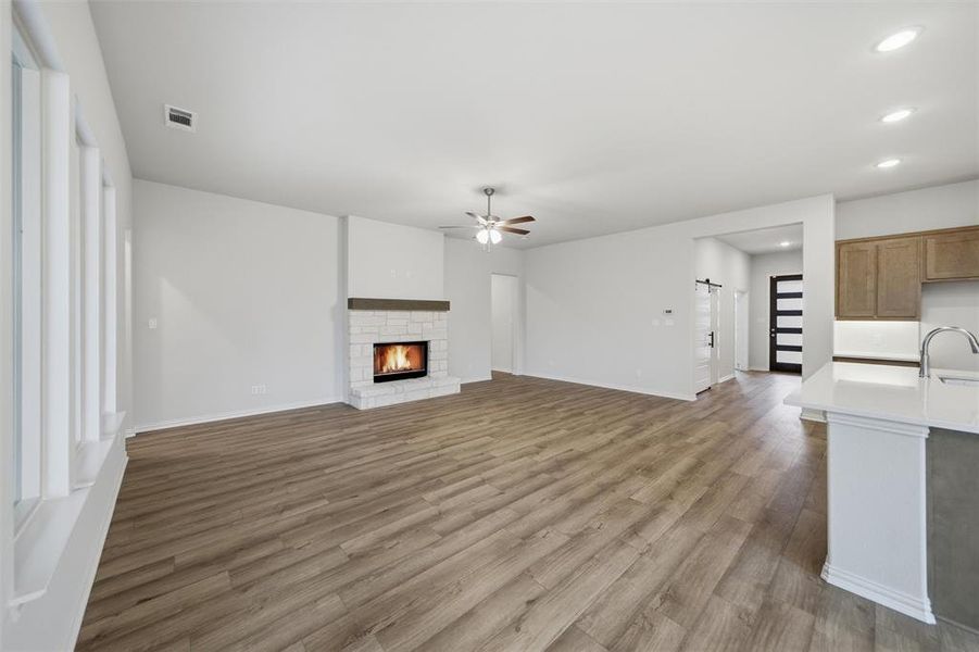 Unfurnished living room with ceiling fan, a warm lit fireplace, light wood-type flooring, and recessed lighting Unfurnished living room with ceiling fan, a warm lit fireplace, light wood-type flooring, and recessed lighting