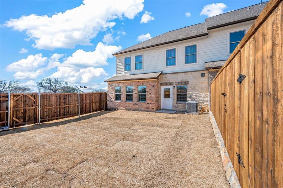 Back of property featuring a shingled roof, a fenced backyard, brick siding, and central AC