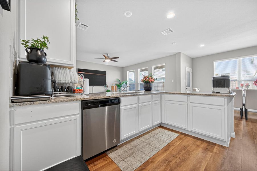 Bright and spacious kitchen with white cabinetry, granite countertops, and stainless steel appliances. The open layout connects to a living area with large windows, offering ample natural light.