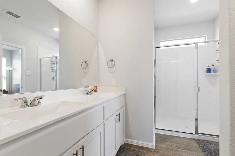 Full bathroom with healthy amount of natural light, a shower stall, double vanity, dark wood-style flooring, and recessed lighting