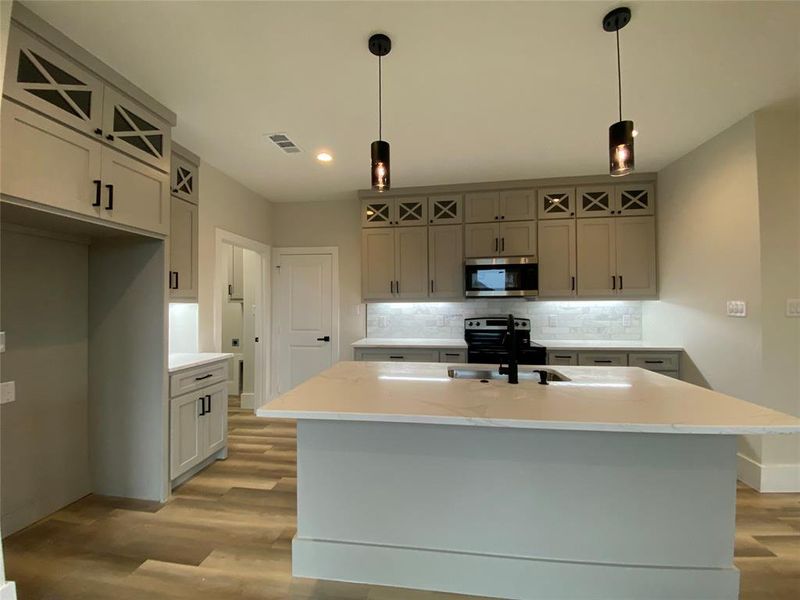 Kitchen with a center island with sink, light wood-type flooring, appliances with stainless steel finishes, and tasteful backsplash