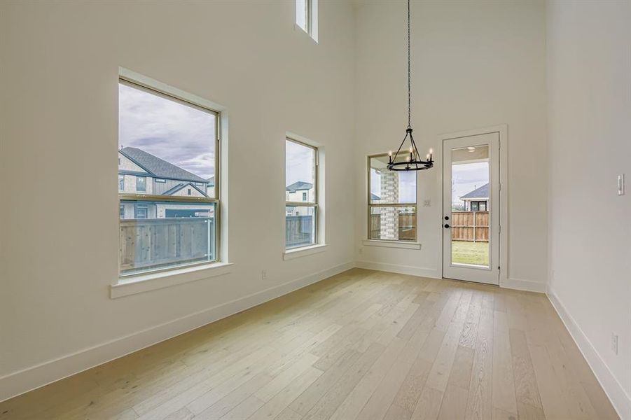 Unfurnished dining area featuring light wood-style floors, a chandelier, and a high ceiling Unfurnished dining area featuring light wood-style floors, a chandelier, and a high ceiling
