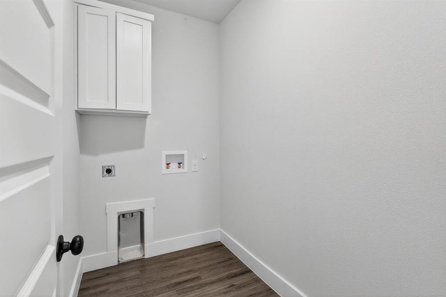 Laundry space featuring a paneled door with a black knob, wood-finish flooring, white baseboards, and a built-in white shaker-style cabinet