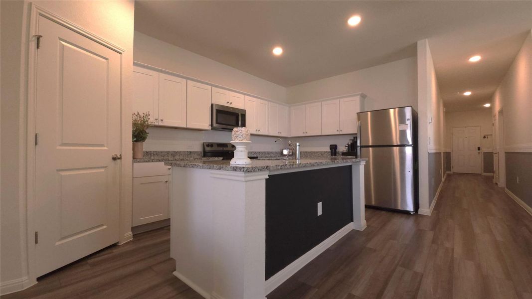 Kitchen featuring wood-finish flooring, white cabinetry, granite countertops, and stainless steel appliances