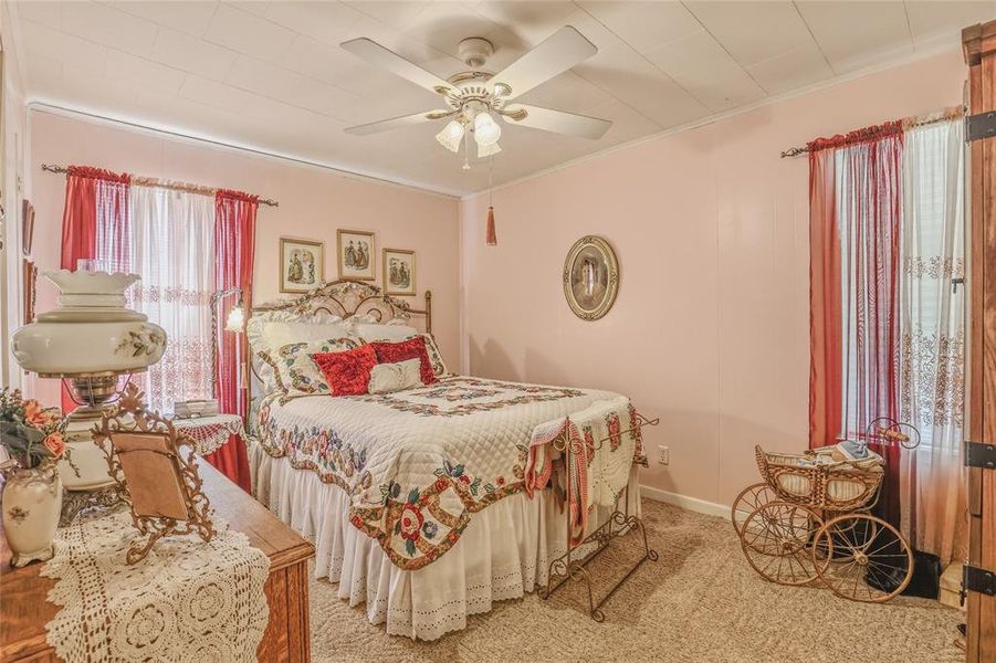 Carpeted room featuring a ceiling fan with integrated lighting, a window with curtain rod and sheer and opaque drapes, and light pink wall paneling Carpeted room featuring a ceiling fan with integrated lighting, a window with curtain rod and sheer and opaque drapes, and light pink wall paneling