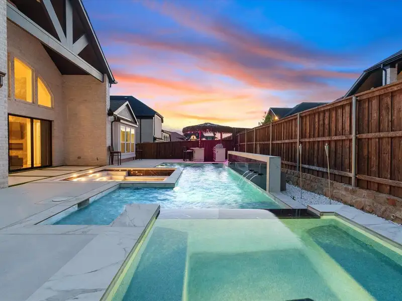 Expansive pool area featuring multiple water features, integrated spa, and a light-colored paver patio Expansive pool area featuring multiple water features, integrated spa, and a light-colored paver patio