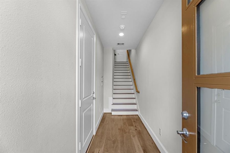 As you step into the townhome, you're greeted by gleaming wood floors and crisp white walls that create a bright and inviting atmosphere. The elegant wooden staircase ahead leads gracefully upward, while a private garage entrance is conveniently located to the left.