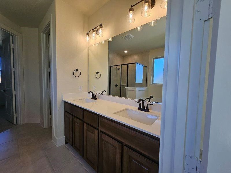 Bathroom featuring double vanity, a stall shower, and light tile patterned flooring