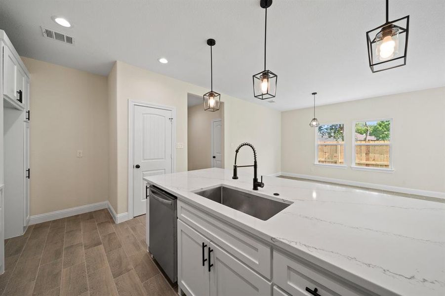 Kitchen with light stone counters, white cabinetry, hanging light fixtures, sink, and wood-type flooring