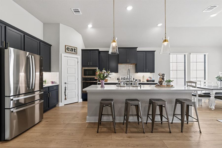 This modern kitchen features sleek dark navy cabinetry, a large central island with seating, stainless steel appliances, and stylish pendant lighting.