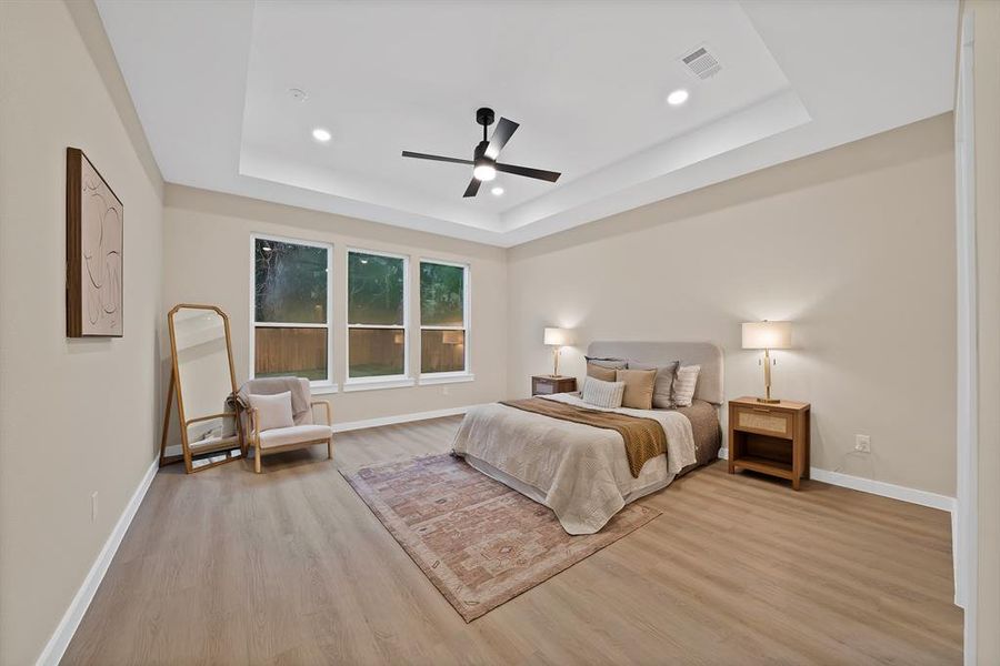 Spacious room featuring a tray ceiling with recessed lighting, a ceiling fan, wood-finish flooring, and three large windows Spacious room featuring a tray ceiling with recessed lighting, a ceiling fan, wood-finish flooring, and three large windows