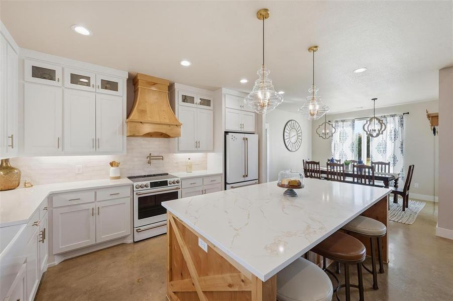 Kitchen with white cabinetry, tasteful backsplash, white appliances, a center island, and hanging light fixtures Kitchen with white cabinetry, tasteful backsplash, white appliances, a center island, and hanging light fixtures