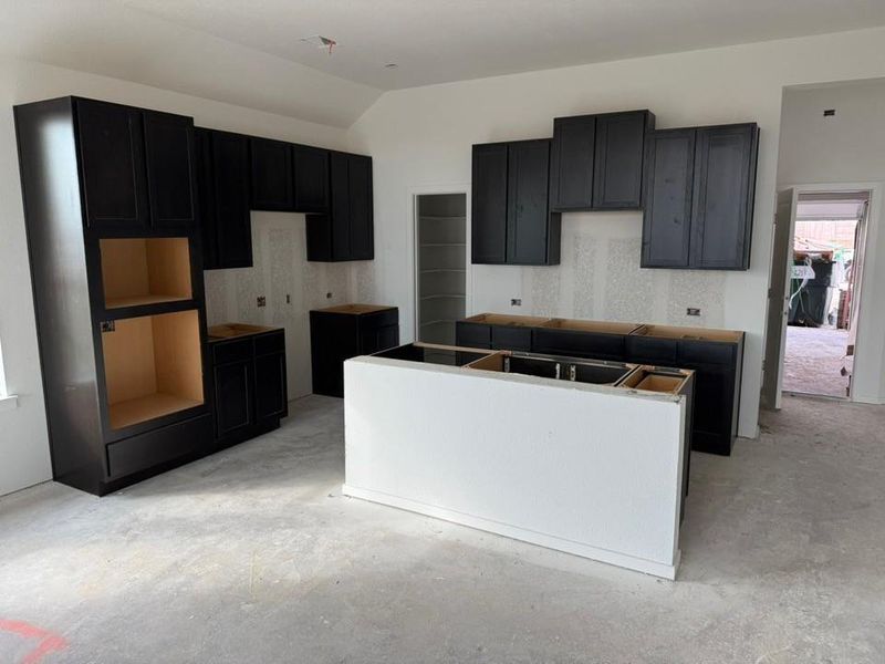 Kitchen featuring a center island, unfinished concrete floors, dark cabinetry, and lofted ceiling